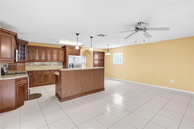 kitchen with appliances with stainless steel finishes, glass insert cabinets, brown cabinets, decorative light fixtures, and a center island