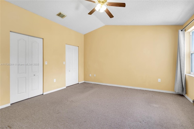 carpeted empty room featuring lofted ceiling, a textured ceiling, visible vents, and baseboards