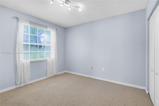 empty room featuring light carpet, a textured ceiling, and baseboards