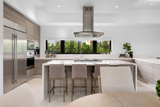 kitchen with light tile patterned floors, a breakfast bar area, stainless steel appliances, a center island, and island exhaust hood