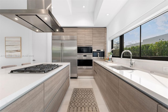 kitchen with built in appliances, sink, light tile patterned floors, and island exhaust hood