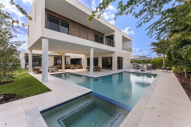 rear view of house featuring a swimming pool with hot tub, a balcony, and a patio area