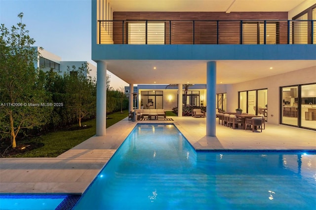 pool at dusk with a patio area and outdoor lounge area