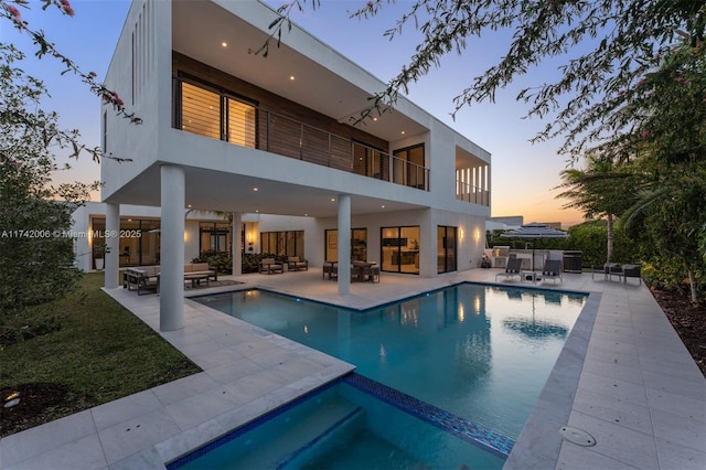 back house at dusk featuring a patio, a balcony, and outdoor lounge area