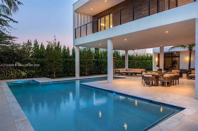 pool at dusk with outdoor lounge area and a patio