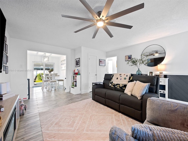 living room featuring ceiling fan, light wood-type flooring, and a textured ceiling