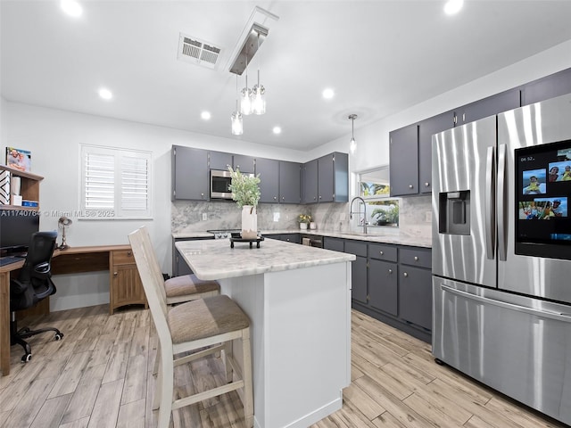 kitchen with gray cabinetry, decorative light fixtures, a center island, stainless steel appliances, and light stone countertops