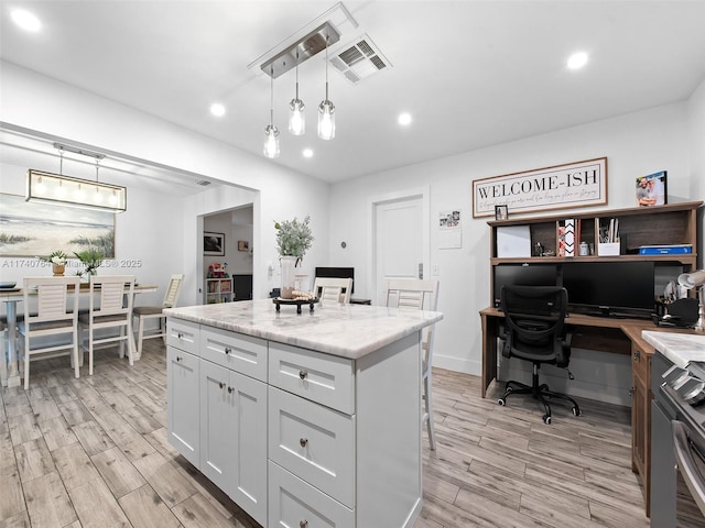 kitchen with decorative light fixtures, a kitchen breakfast bar, a kitchen island, light stone countertops, and light hardwood / wood-style floors