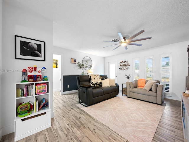 living room featuring ceiling fan, a textured ceiling, and light wood-type flooring