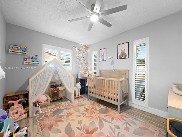 bedroom featuring hardwood / wood-style flooring, ceiling fan, a nursery area, and a textured ceiling