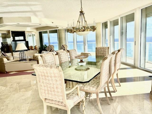 dining space featuring a water view, plenty of natural light, a textured ceiling, and a chandelier