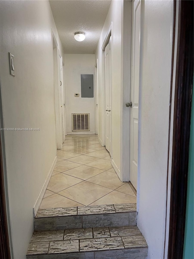 corridor featuring electric panel, light tile patterned floors, and a textured ceiling