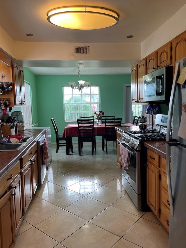 kitchen featuring decorative light fixtures, a notable chandelier, sink, light tile patterned floors, and appliances with stainless steel finishes