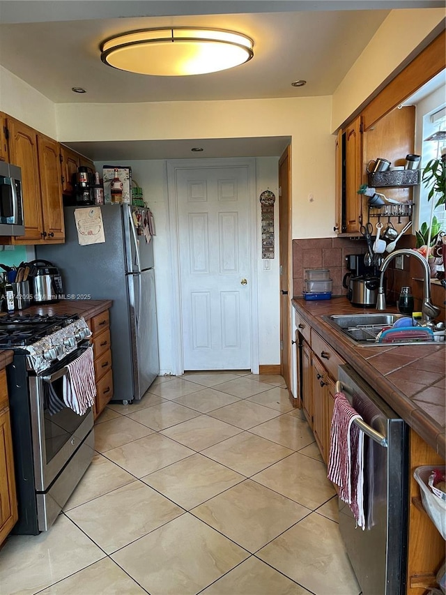 kitchen featuring tasteful backsplash, stainless steel appliances, tile counters, light tile patterned flooring, and sink