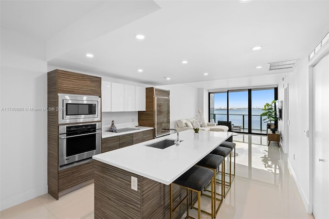 kitchen featuring appliances with stainless steel finishes, white cabinetry, sink, a kitchen island with sink, and a water view