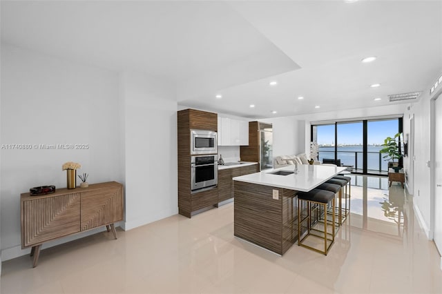 kitchen featuring sink, white cabinetry, stainless steel appliances, a water view, and a center island with sink