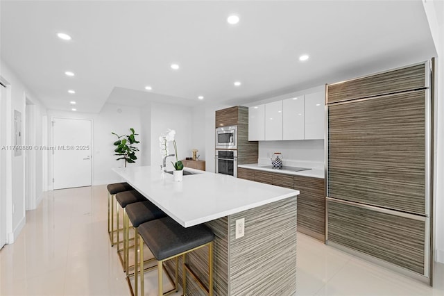 kitchen featuring sink, a breakfast bar area, appliances with stainless steel finishes, a kitchen island with sink, and white cabinets