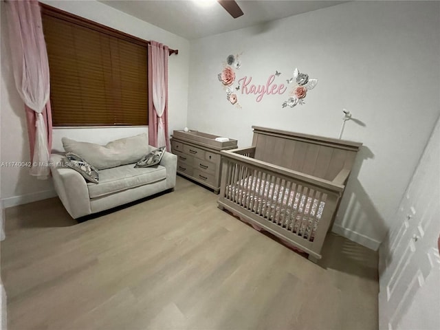 bedroom with a crib, ceiling fan, and light hardwood / wood-style floors