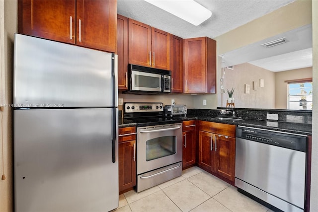 kitchen featuring sink, a textured ceiling, dark stone countertops, light tile patterned floors, and appliances with stainless steel finishes