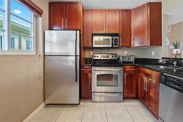 kitchen with sink, dark stone countertops, light tile patterned floors, stainless steel appliances, and a textured ceiling