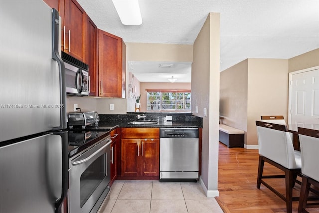 kitchen featuring appliances with stainless steel finishes, sink, dark stone counters, light tile patterned floors, and a textured ceiling