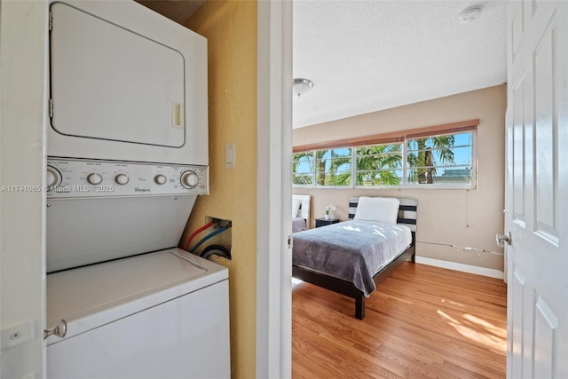 washroom featuring light hardwood / wood-style flooring, stacked washer and clothes dryer, and a textured ceiling