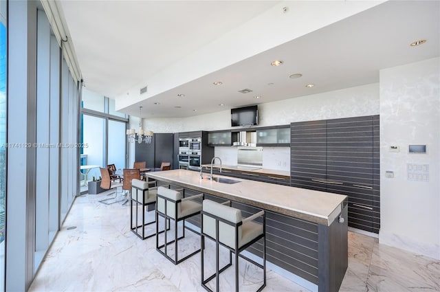 kitchen with sink, a wall of windows, a kitchen breakfast bar, a notable chandelier, and a center island with sink