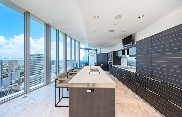 kitchen featuring sink, a kitchen island with sink, black electric stovetop, a notable chandelier, and floor to ceiling windows