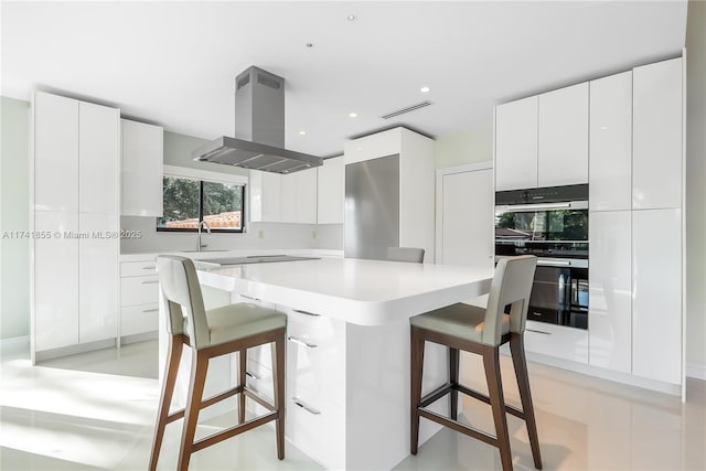 kitchen featuring a breakfast bar, modern cabinets, stainless steel double oven, and island range hood