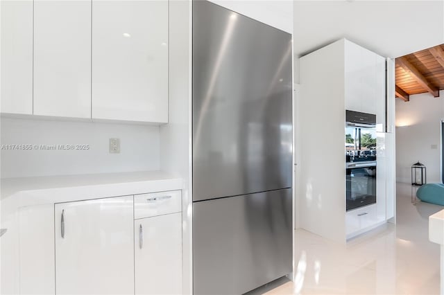 kitchen with beamed ceiling, white cabinetry, wooden ceiling, and stainless steel refrigerator