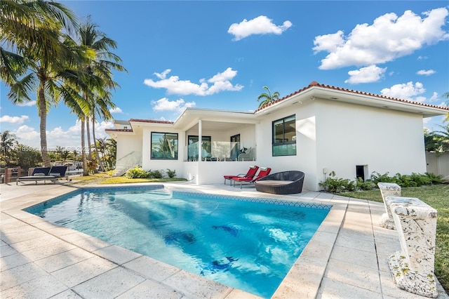 rear view of property with a patio area, stucco siding, a tiled roof, and an outdoor pool