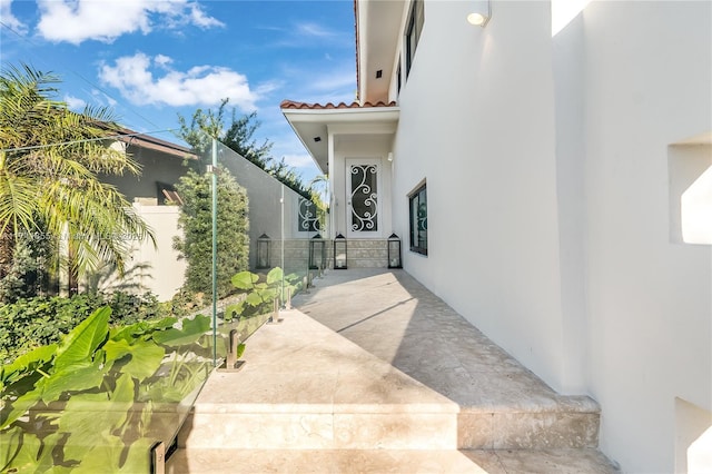 entrance to property featuring a tiled roof, stucco siding, and fence