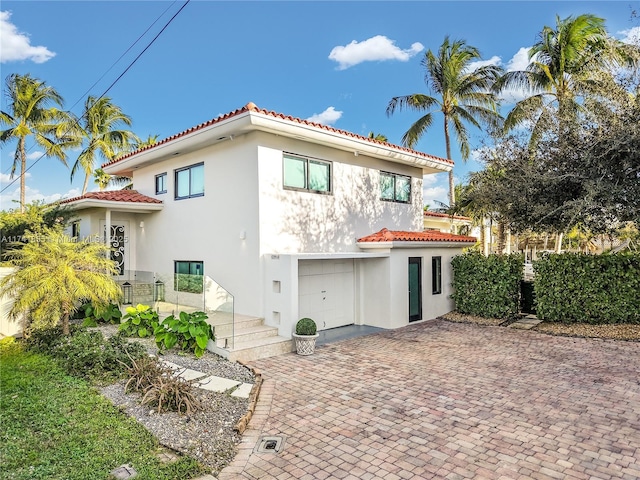 rear view of house featuring a tiled roof, decorative driveway, a garage, and stucco siding