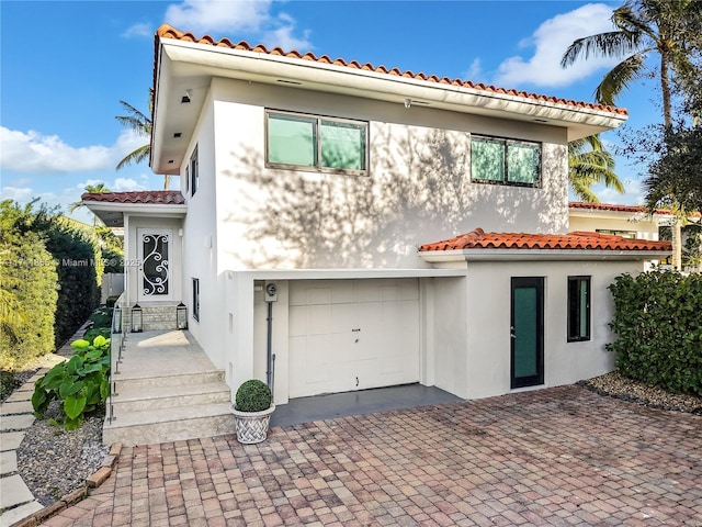 view of front of property featuring stucco siding, a tile roof, a garage, and decorative driveway