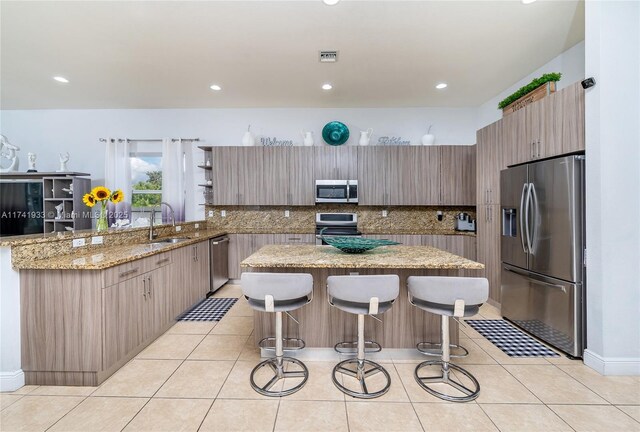 kitchen with appliances with stainless steel finishes, a kitchen island, tasteful backsplash, light stone countertops, and a kitchen bar