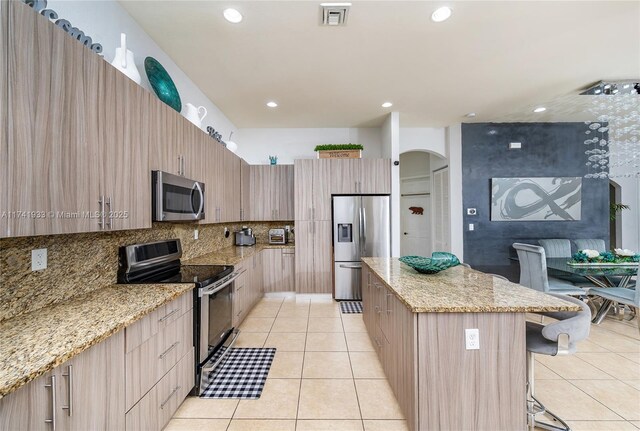 kitchen featuring a kitchen bar, light tile patterned floors, light stone countertops, and appliances with stainless steel finishes