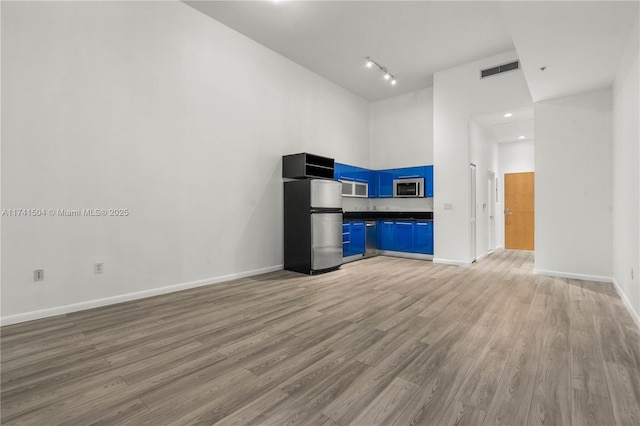 unfurnished living room featuring rail lighting, a towering ceiling, and light hardwood / wood-style flooring