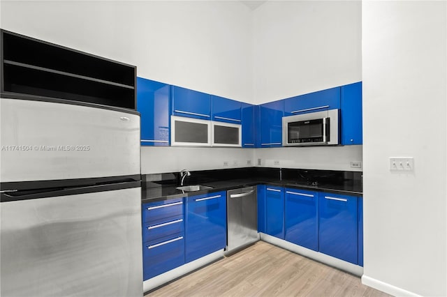 kitchen featuring sink, blue cabinetry, stainless steel appliances, light hardwood / wood-style floors, and dark stone counters