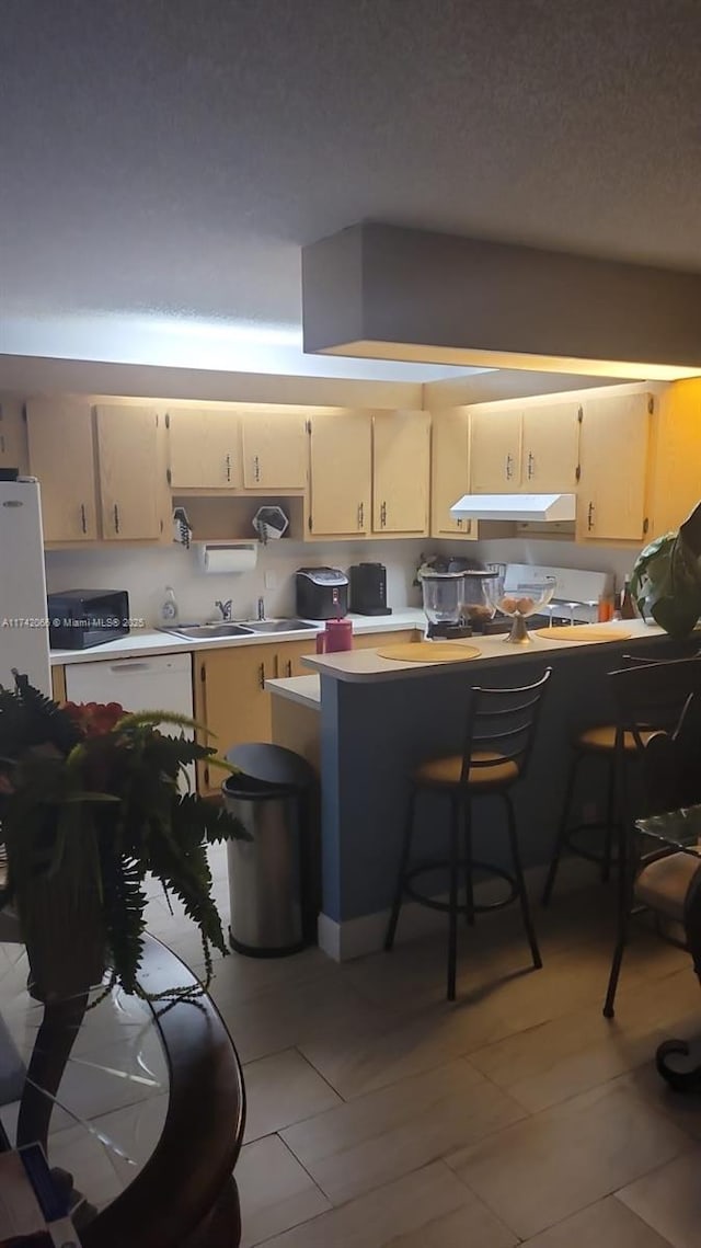 kitchen featuring cream cabinets, light tile patterned floors, a kitchen breakfast bar, and a textured ceiling