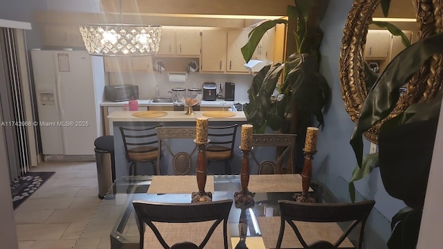 kitchen with sink, light tile patterned floors, a notable chandelier, white refrigerator with ice dispenser, and cream cabinetry