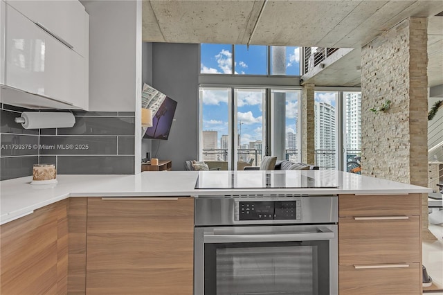 kitchen with black electric stovetop, wall oven, kitchen peninsula, and backsplash