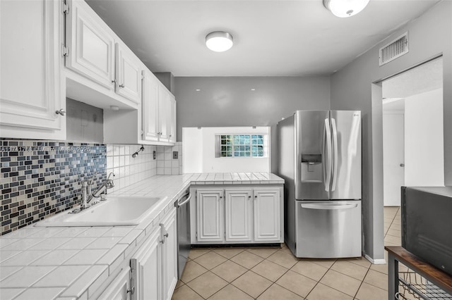 kitchen with white cabinetry, stainless steel appliances, tile counters, and sink