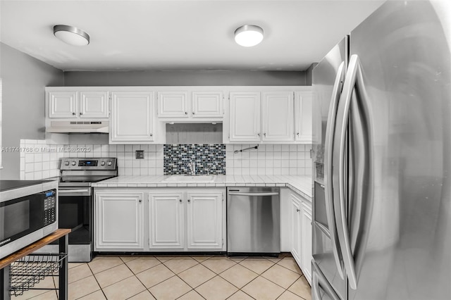 kitchen with stainless steel appliances, light tile patterned floors, decorative backsplash, and white cabinets