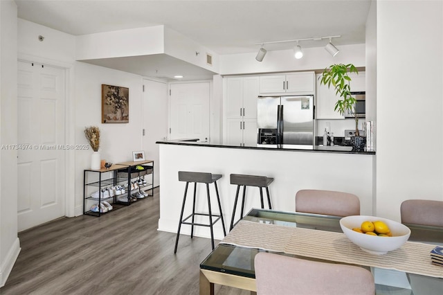 kitchen featuring wood finished floors, white cabinetry, stainless steel refrigerator with ice dispenser, dark countertops, and a kitchen bar