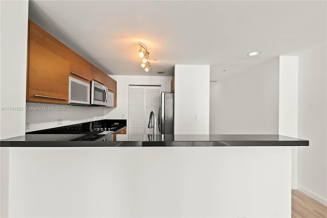 kitchen with stainless steel appliances, sink, light wood-type flooring, and kitchen peninsula