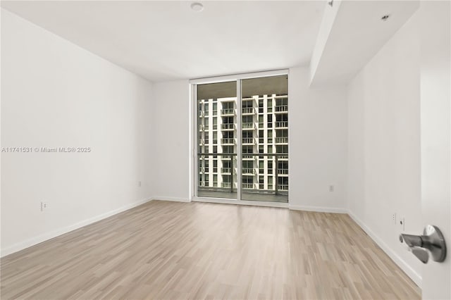 empty room with floor to ceiling windows and light hardwood / wood-style floors