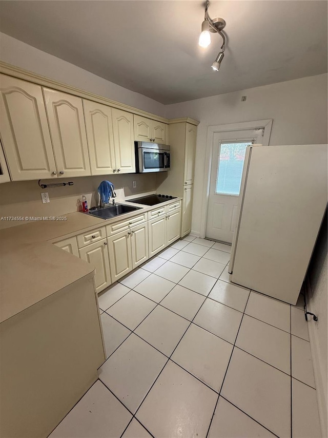 kitchen with light tile patterned flooring, sink, white refrigerator, black electric stovetop, and cream cabinets