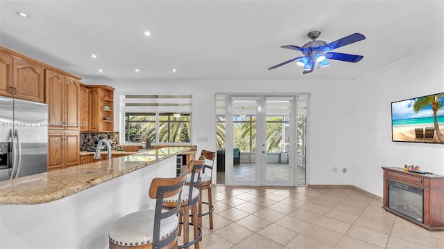 kitchen featuring light tile patterned floors, stainless steel fridge, a breakfast bar, light stone counters, and decorative backsplash