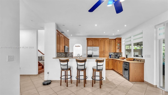 kitchen with appliances with stainless steel finishes, beverage cooler, a kitchen bar, decorative backsplash, and kitchen peninsula