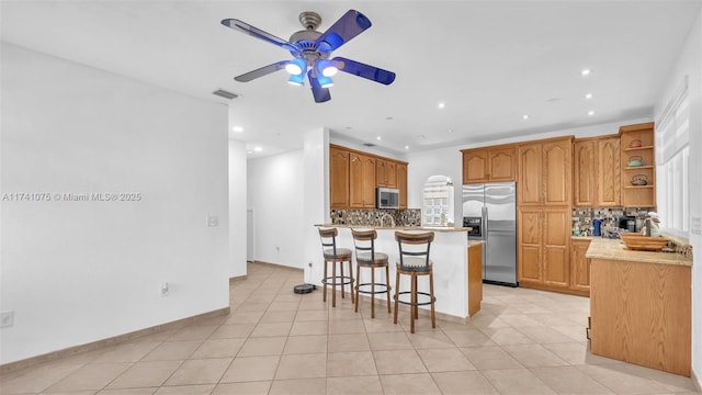 kitchen featuring a breakfast bar, decorative backsplash, a center island, ceiling fan, and stainless steel appliances